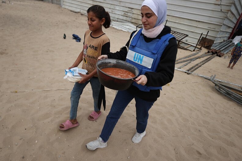 Ein Kind und eine WFP-Mitarbeiterin im Gazastreifen tragen Nahrungsmittel. © WFP