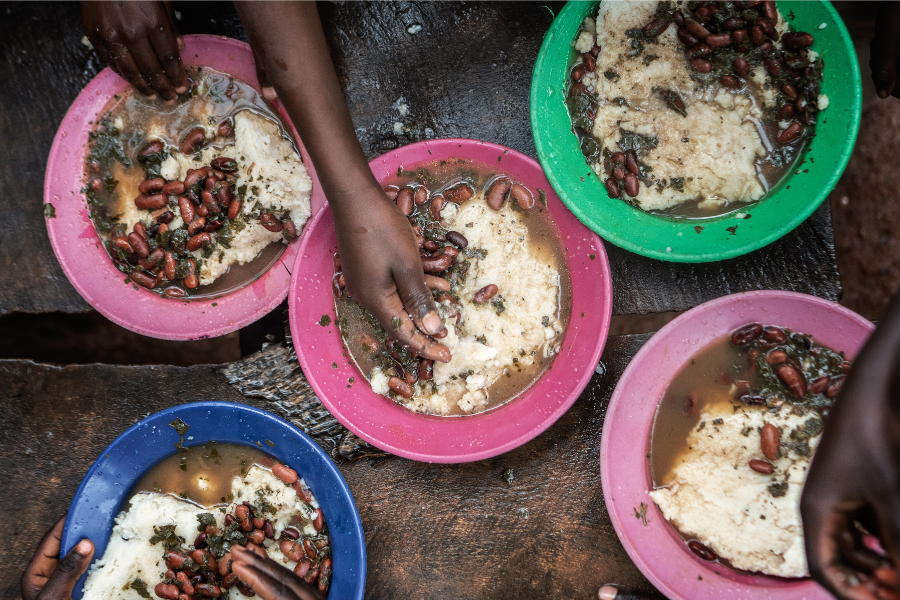 Children's hands reach into bowls filled with school meals in Burundi.