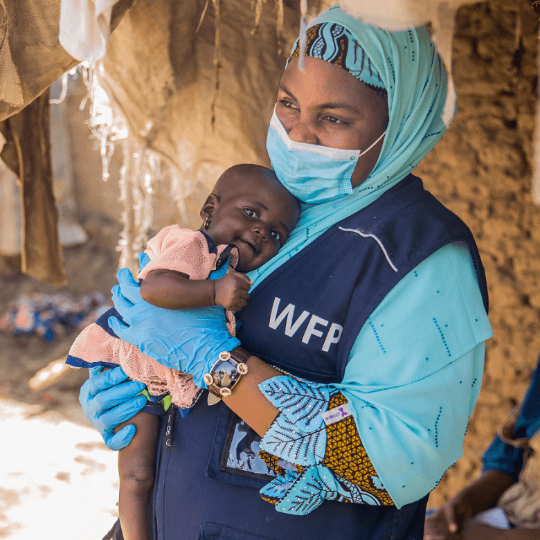 A WFP staff member holds 10-month-old Hassana after WFP treatment for malnutrition. Hassana is one of a set of twins whose parents were uprooted by conflict in northeast Nigeria and then struggled to earn enough money because of the COVID-19 pandemic.