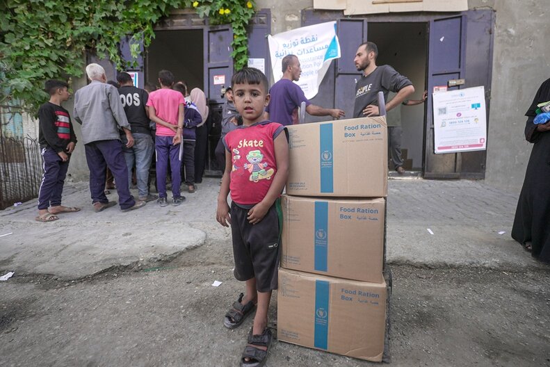 Ein Kind steht neben WFP-Lebensmittelpaketen in Gaza.