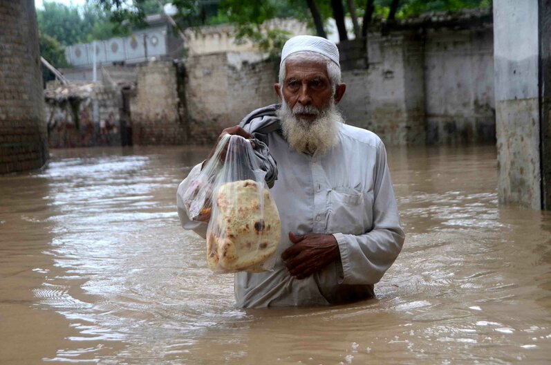 Auf diesem Foto watet ein Mann mit Brot durch ein überschwemmtes Gebiet in Peshawar, Khyber Pakhtunkhwa, Pakistan. Tausende von Menschen, die in von Überschwemmungen gefährdeten Gebieten leben, wurden aufgefordert, diese zu verlassen. Bildnachweis: Hussain Ali / ANADOLU AGENCY / Anadolu Agency via AFP 