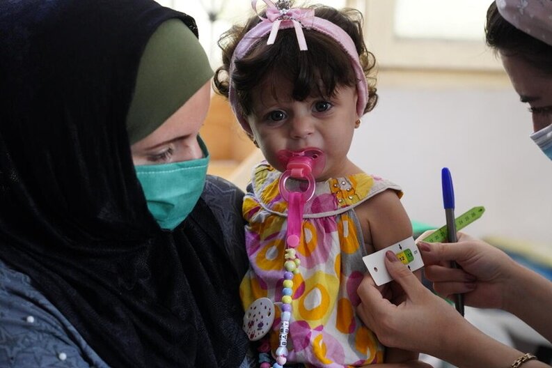 Bei einem Kind, das von seiner Mutter gehalten wird, wird der Umfang des mittleren Oberarms im Rahmen eines Ernährungsscreenings in einer vom WFP unterstützten Klinik gemessen.