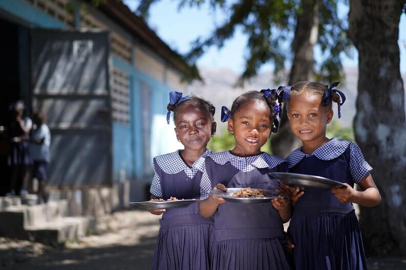 Drei Mädchen in Schuluniform in Haiti, die eine Schulmahlzeit in den Händen halten. WFP verteilt täglich warme Mahlzeiten an 250.000 Kinder in Haiti.