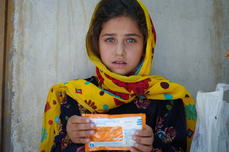 Ein Mädchen welches eine Packung angereicherte Erdnusspaste zur Behandlung von Mangelernährung in die Kamera hält. © WFP/Mohammad Hasib Hazinyar