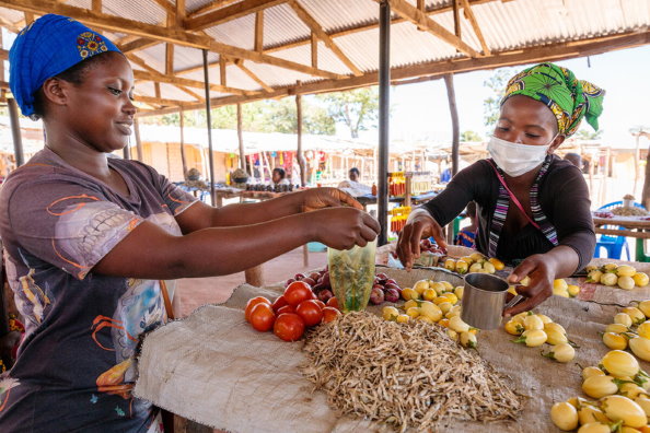 WFP/Andy Higgins. Sambia. Mulumbwa, eine geflüchtete Frau aus der DRK, bedient eine Kundin an ihrem Marktstand