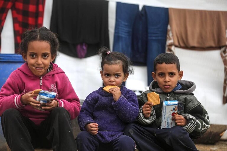 Three children sat and eating WFP biscuits.