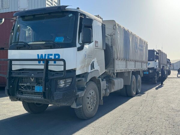WFP trucks loaded with food supplies line up on a paved road, forming a convoy ready to deliver humanitarian assistance.