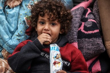 Ein kleiner Junge mit lockigen Haaren, welcher einen von WFP bereitgestellten Keks isst.