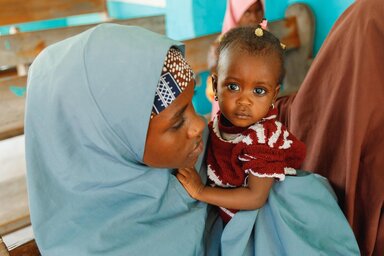 Eine Mutter und ihr Baby am Eingang des Gesundheitszentrums, die zum ersten Mal zu Besuch kommen, als bei ihrem Kind schwere akute Unterernährung (SAM) diagnostiziert wird.