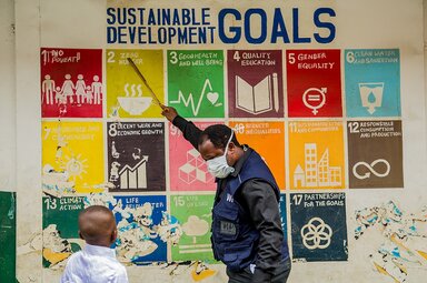 Ein Mitarbeiter des Welternährungsprogramms (WFP) unterrichtet David in einem Verteilungszentrum für das nationale Schulspeisungsprogramm in der Adekunle Anglican Primary School, Makoko, Lagos, Nigeria, über die Ziele für nachhaltige Entwicklung.