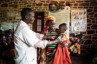 Burundi. Goretti holds her baby Schola while the nurse rolls a MUAC tape around her arm.