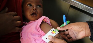 Ein kleines Mädchen wird in einer vom WFP unterstützten Klinik in Nord-Kordofan mit dem MUAC-Test (Mid Upper Arm Circumference) auf Unterernährung untersucht und erhält vom WFP angereicherte Spezialnahrung.