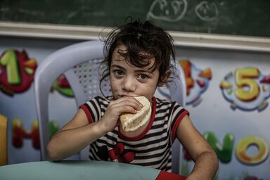 Ein junges Mädchen isst Brot, das vom Welternährungsprogramm (WFP) in einer UNRWA-Schule verteilt wurde, die in Notzeiten als Schutzraum dient.