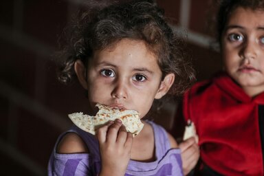 © WFP/Ali Jadallah Ein kleines Mädchen isst Brot und blickt in die Kamera.