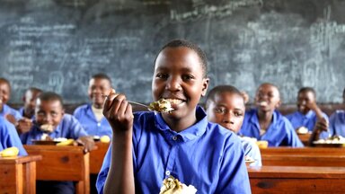 A child at a school desk with a fork-full of food