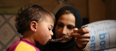 Ein Kind welches von seiner Mutter gefüttert wird.