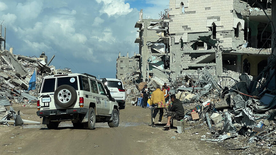 UN vehicles drive past destroyed buildings as Gazans walk past