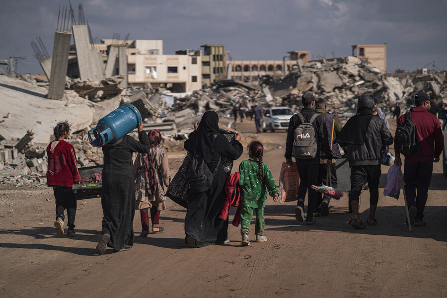 Adults and children walk down a road surrounded by rocket-struck buildings