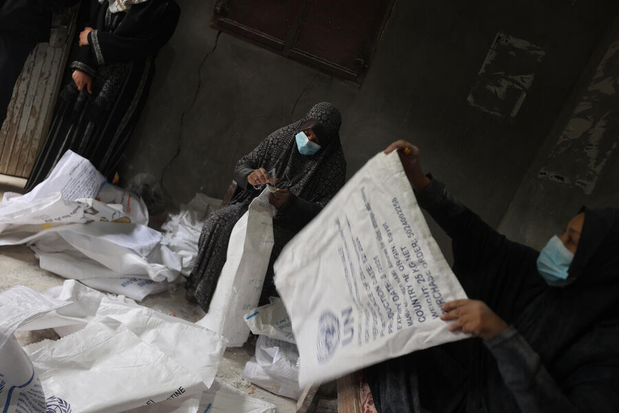 A woman sews in a room filled with white food bags, one of which, held up to the camera, bears the blue UN logo