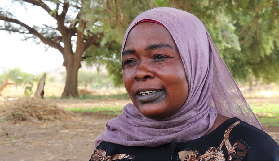 Headshot of a smiling woman in a purple headscarf with trees and fields in the background. Photo: WFP/Petroc Wilton