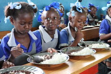 Foto: WFP/Alexis Masciarelli. Schülerinnen und Schüler im Alter von 5 bis 7 Jahren essen eine warme Mahlzeit in ihrem Klassenzimmer der Grundschule Baptiste Salem in Dondon, an der 600 Kinder registriert sind. Die Mahlzeiten werden täglich mit Reis und Bohnen zubereitet – Lebensmittel, die über das WFP-Programm für lokal produzierte Schulmahlzeiten von lokalen Produzenten gekauft werden.