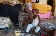 WFP/Abubaker Garelnabei, Eine Frau trägt ein kleines Mädchen. Ihre Mutter ist auf der Suche nach Arbeit, um die Familie zu ernähren