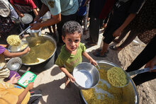 WFP/Ali Jadallah. Auf dem Foto erhalten und essen die Kinder Reis, den sie aus einer nahe gelegenen, vom WFP unterstützten Küche für warme Mahlzeiten mitgebracht haben. Die Kinder warteten oft stundenlang geduldig auf diese Mahlzeit. In der Regel brachten sie das Essen zurück in das Zelt der Familie. Gaza, Palästina.